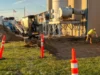 An image of two construction workers and a small excavator working outside a commercial building.
